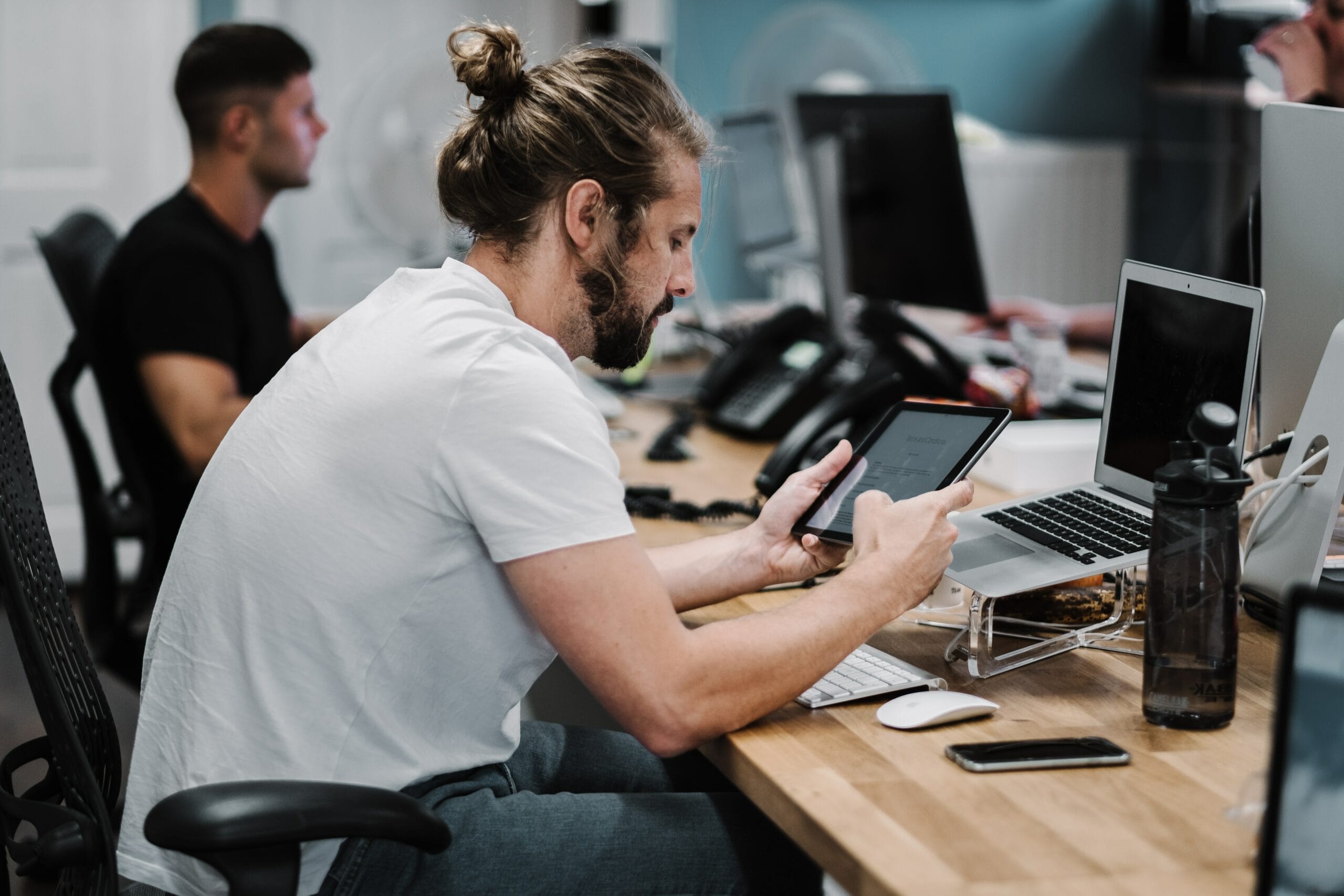 Bearded man at a desk using a tablet and laptop in an office, symbolizing solutions to medical data management challenges.